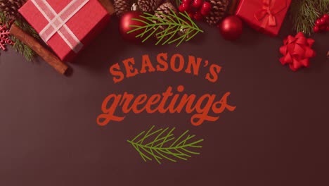 Animation-of-seasons-greetings-text-banner-with-leaves-icon-over-christmas-decorations-and-gifts