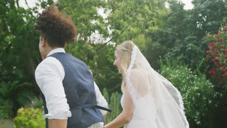 Happy-diverse-couple-walking-in-garden-on-sunny-day-at-wedding