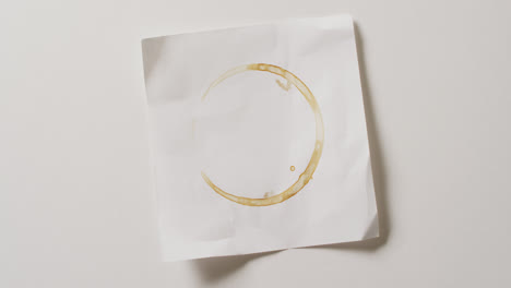 Video-of-close-up-of-piece-of-paper-with-coffee-mug-stain-on-white-background