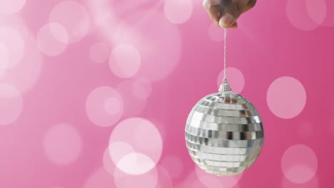 Animation-of-silver-bauble-and-white-spots-of-light-on-pink-background