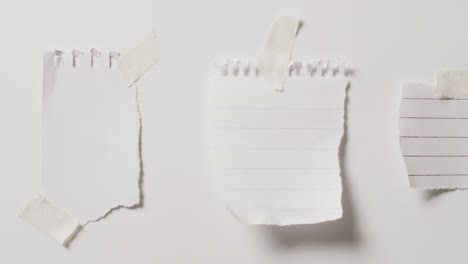 Video-of-close-up-of-three-scraps-of-paper-with-copy-space-taped-on-white-background