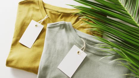 Video-of-close-up-of-folded-green-and-mustard-t-shirts-with-tags-on-white-background