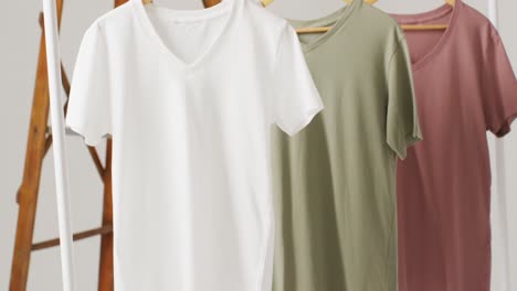 Video-Einer-Nahaufnahme-Von-T-Shirts-In-Weiß,-Beige-Und-Grün,-Die-Auf-Weißem-Hintergrund-Hängen