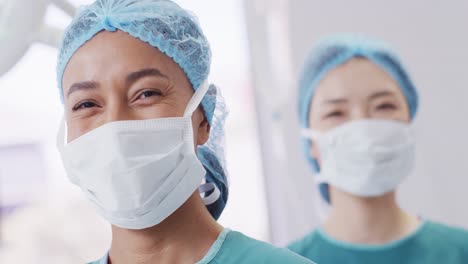 Portrait-of-smiling-biracial-female-surgeon-in-cap-and-face-mask-in-operating-theatre,-copy-space