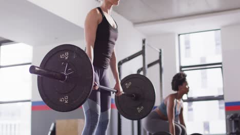 Video-of-two-diverse,-determined-women-lifting-barbell-weights-working-out-at-a-gym