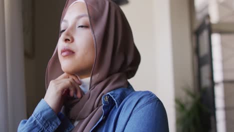 Vídeo-De-Una-Mujer-Birracial-Pensativa-Con-Hijab-Mirando-Por-La-Ventana-De-Su-Casa