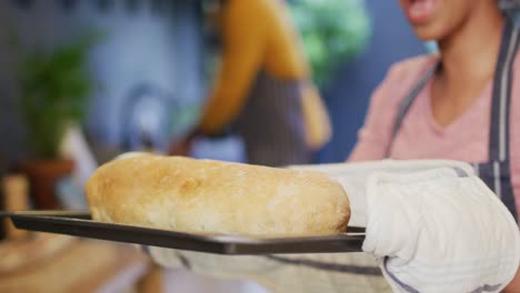 Video-of-happy-diverse-couple-baking,-woman-taking-bread-out-of-oven-in-kitchen,-with-copy-space