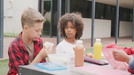 Video-of-two-diverse-schoolboys-eating-packed-lunch-and-talking-in-schoolyard
