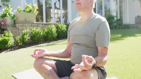 Glücklicher-Kaukasischer-älterer-Mann,-Der-Yoga-Praktiziert-Und-Auf-Einer-Matte-Im-Garten-Meditiert