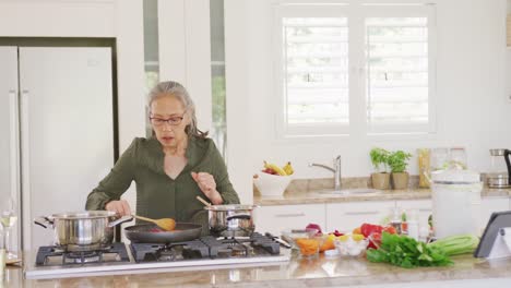 Glückliche-Asiatische-ältere-Frau,-Die-Ein-Tablet-Benutzt-Und-In-Der-Küche-Kocht