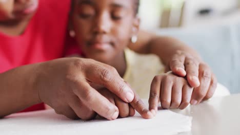 Video-of-hands-of-african-american-grandmother-helping-granddaughter-read-braille