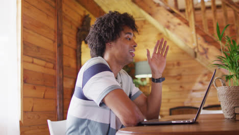 Happy-african-american-man-sitting-at-table-and-using-laptop-for-video-call,-slow-motion