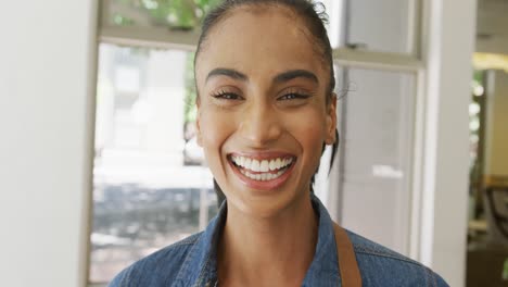 Portrait-of-happy-biracial-female-barista-laughing-in-her-coffee-shop
