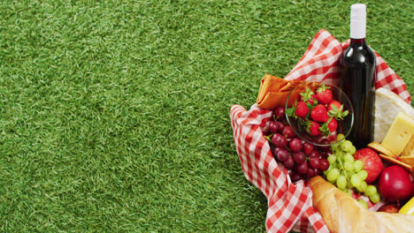 Picnic-basket-with-checkered-blanket,-fruits,-bread,-cheese-and-wine-on-grass-with-copy-space