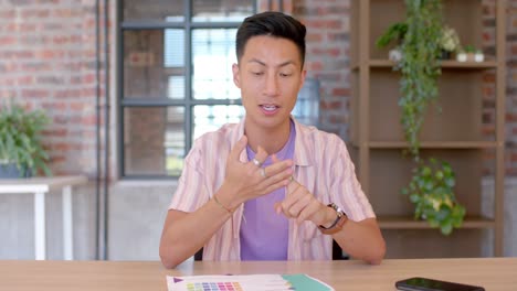 Happy-asian-man-talking-and-gesturing-during-casual-work-video-call,-slow-motion,-copy-space