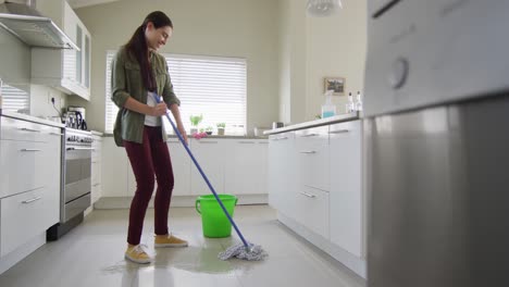 Happy-caucasian-woman-cleaning-floor-with-mop-and-bucket-of-water-at-home