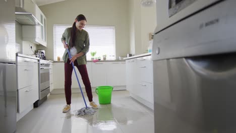 Happy-caucasian-woman-cleaning-floor-with-mop-and-bucket-of-water-at-home