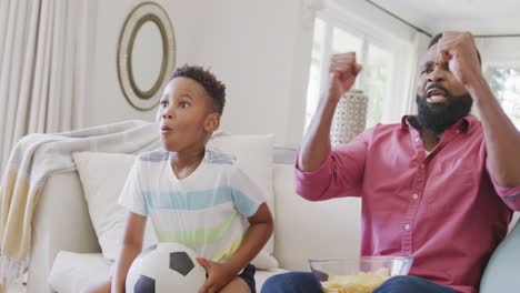 Happy-african-american-father-and-son-watching-football-match-and-supporting,-in-slow-motion