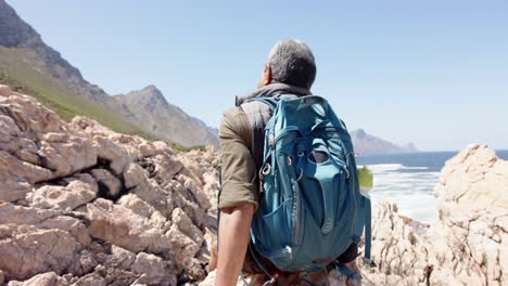 Senior-biracial-man-in-mountains-resting-at-sea,-in-slow-motion