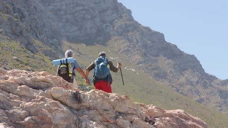 Pareja-Birracial-Senior-En-Montañas-Caminando-Con-Bastones-De-Trekking,-En-Cámara-Lenta
