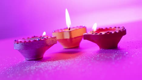 Close-up-of-burning-colourful-candles-celebrating-diwali-on-purple-background