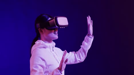 Asian-woman-using-vr-headset,-touching-virtual-screen-on-blue-background,-slow-motion