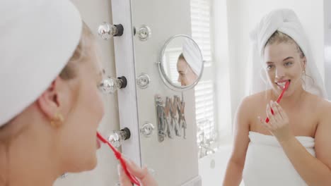 Happy-caucasian-plus-size-woman-in-front-of-mirror-with-towel-on-head-brushing-teeth-in-slow-motion