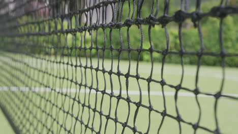 Close-up-of-tennis-net-and-ball-on-tennis-court-in-garden-on-sunny-day
