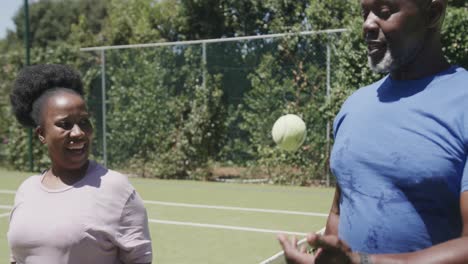 Happy-senior-african-american-couple-playing-tennis-and-high-fiving-at-tennis-court-in-slow-motion