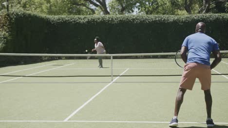 Happy-senior-african-american-couple-playing-tennis-at-tennis-court-in-slow-motion