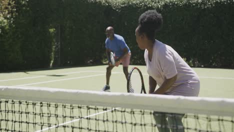 Happy-senior-african-american-couple-playing-tennis-at-tennis-court-in-slow-motion