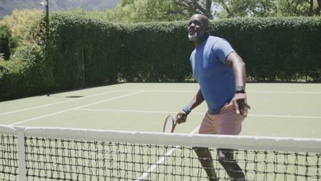 Happy-senior-african-american-man-playing-tennis-at-tennis-court-in-slow-motion