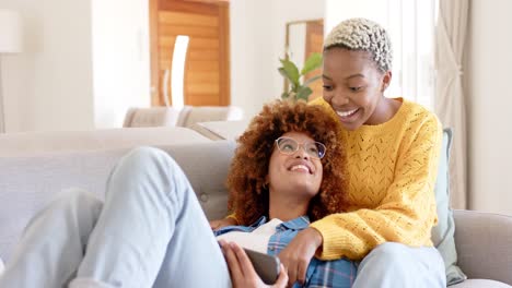 Happy-diverse-female-lesbian-couple-talking-and-using-tablet-in-living-room-in-slow-motion