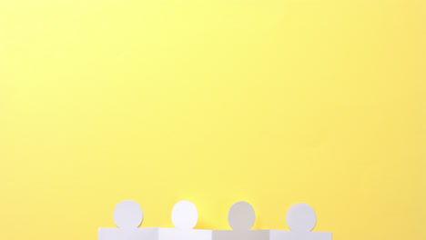 Close-up-of-people-holding-hands-made-of-white-paper-on-yellow-background-with-copy-space