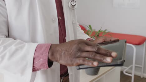 Midsection-of-african-american-male-doctor-wearing-lab-coat,-using-tablet,-slow-motion