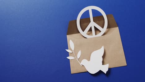 Nahaufnahme-Einer-Weißen-Taube-Mit-Blatt,-Weißem-Friedenszeichen,-Umschlag-Und-Kopierraum-Auf-Blauem-Hintergrund