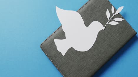 Nahaufnahme-Einer-Weißen-Taube-Mit-Blatt-Auf-Grauem-Notizbuch-Und-Kopierraum-Auf-Blauem-Hintergrund