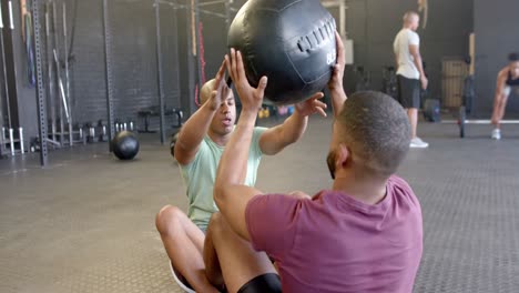 Two-diverse-men-exercising-together,-doing-sit-ups-and-passing-medicine-ball-at-gym,-in-slow-motion