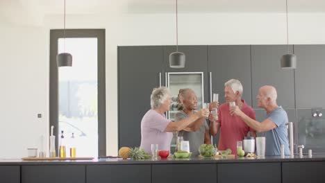 Happy-diverse-senior-friends-making-a-toast-with-health-drinks-in-kitchen,-unaltered,-in-slow-motion