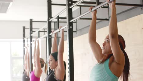 Determined-unaltered-diverse-women-group-training-at-gym-doing-pull-ups-on-bars,-in-slow-motion