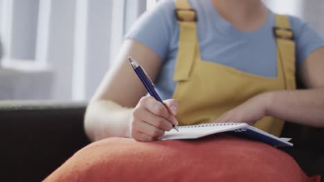 Happy-biracial-woman-taking-notes-and-sitting-on-couch-in-slow-motion