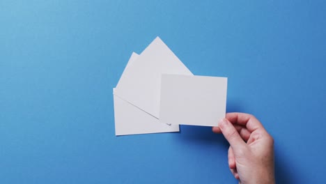 Hand-holding-piece-of-paper-over-pieces-of-paper-with-copy-space-on-blue-background-in-slow-motion