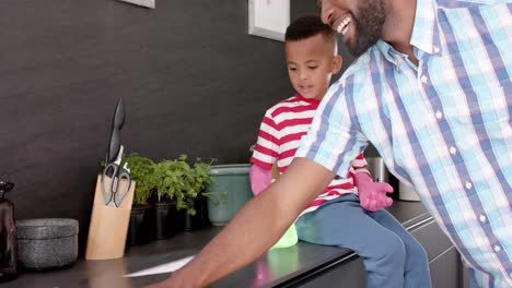 Happy-african-american-father-and-son-cleaning-and-doing-high-five-in-kitchen,-slow-motion