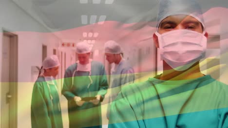 Animation-of-waving-germany-flag-over-biracial-male-surgeon-standing-in-hospital-corridor