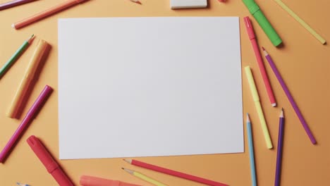 Overhead-view-of-blank-sheet-of-paper-with-school-stationery-on-beige-background,-in-slow-motion