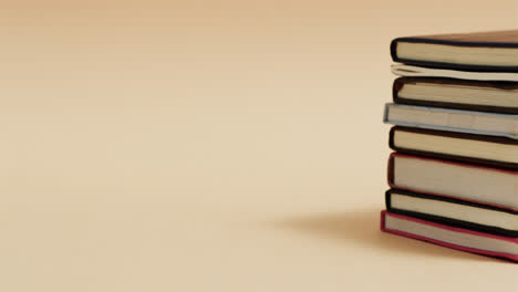 Close-up-of-stack-of-books-with-copy-space-on-beige-background,-in-slow-motion