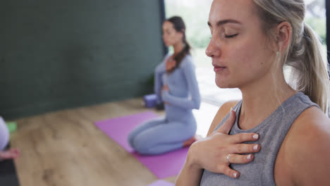Diverse-women-with-hands-on-stomach-and-chest-practicing-breathing-exercise-in-studio