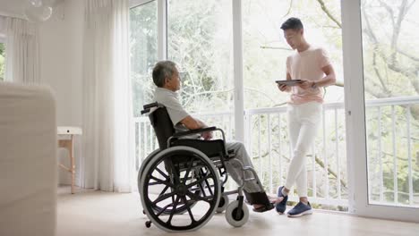Diverser-Männlicher-Physiotherapeut-Mit-Tablet-Beratung-Und-älterer-Mann-Im-Rollstuhl,-In-Zeitlupe