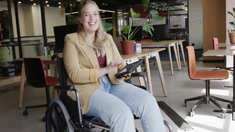 Portrait-of-happy-caucasian-businesswoman-in-wheelchair-using-laptop-in-office,-in-slow-motion