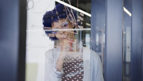 Thoughtful-biracial-casual-businesswoman-making-notes-on-glass-wall,-slow-motion